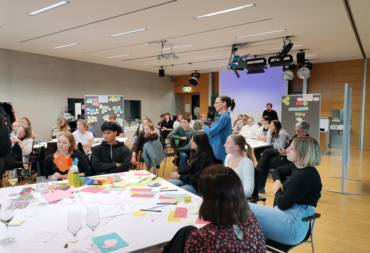Idea Circle Workshop | © ©fachbereich-gestaltung-fhv sitzende Personen um einen Tisch mit vielen bunten Papieren und Präsentationspaneelen | © ©fachbereich-gestaltung-fhv