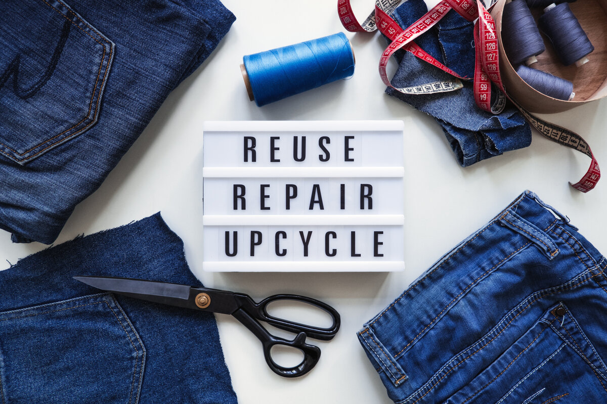 Jeansstücke liegen auf einem Tisch und ein Schild sagt Reuse, Repair, Upcycle. | © AdobeStock