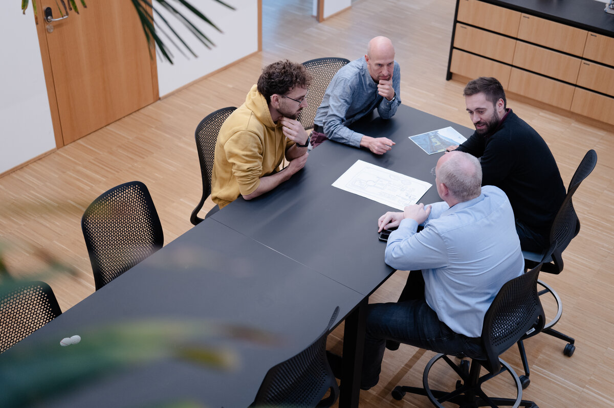 Vier Mitarbeiter des Fachbereichs Technik sitzen an einem Besprechungstisch und besprechen gemeinsam eine technische Zeichnung. | © FHV