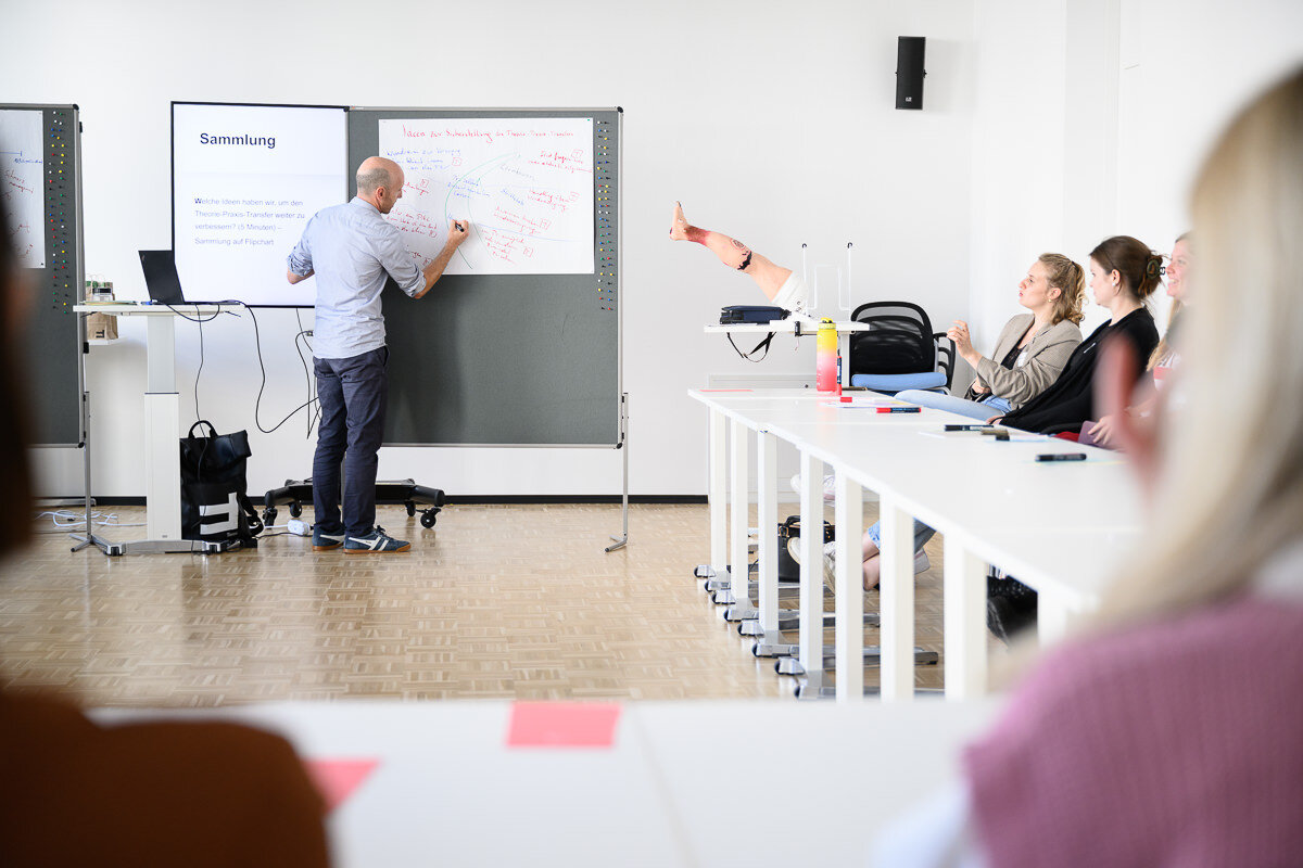 Peter Jäger steht vor eine FlipChart und notiert Begrifflichkeiten. Die Zuhörer hören interessiert zu. | © Matthias Rhomberg | FHV