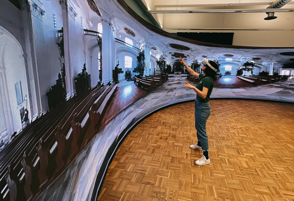 Female person with virtual reality glasses in front of 360 degree video in front of an LED screen | © FHV