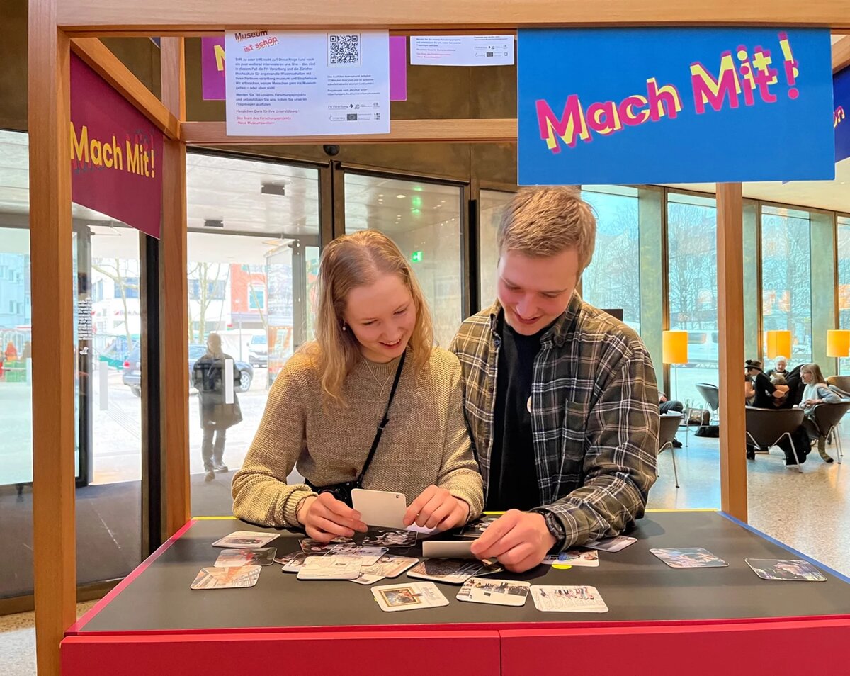 Two people are standing at a stand and playing cards | © FHV