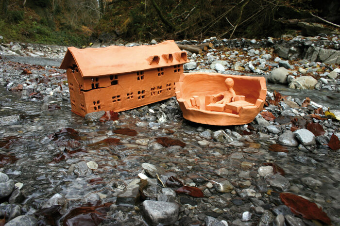 Impression einer Arbeit, die im Rahmen des Forschungsprojekts entstanden ist | © Aqua Mühle Vorarlberg gGmbH Bach mit fliessendem Wasser sowie einem Miniaturtonhaus und einer Miniaturtonperson | © Aqua Mühle Vorarlberg gGmbH
