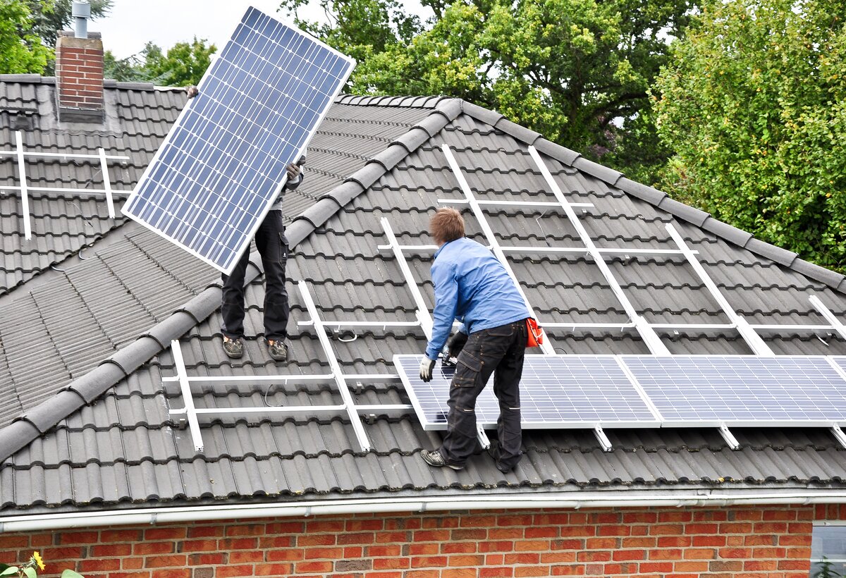 Zwei Männer stehen auf einem Dach und bringen Photovoltaik-Panele an | © AdobeStock