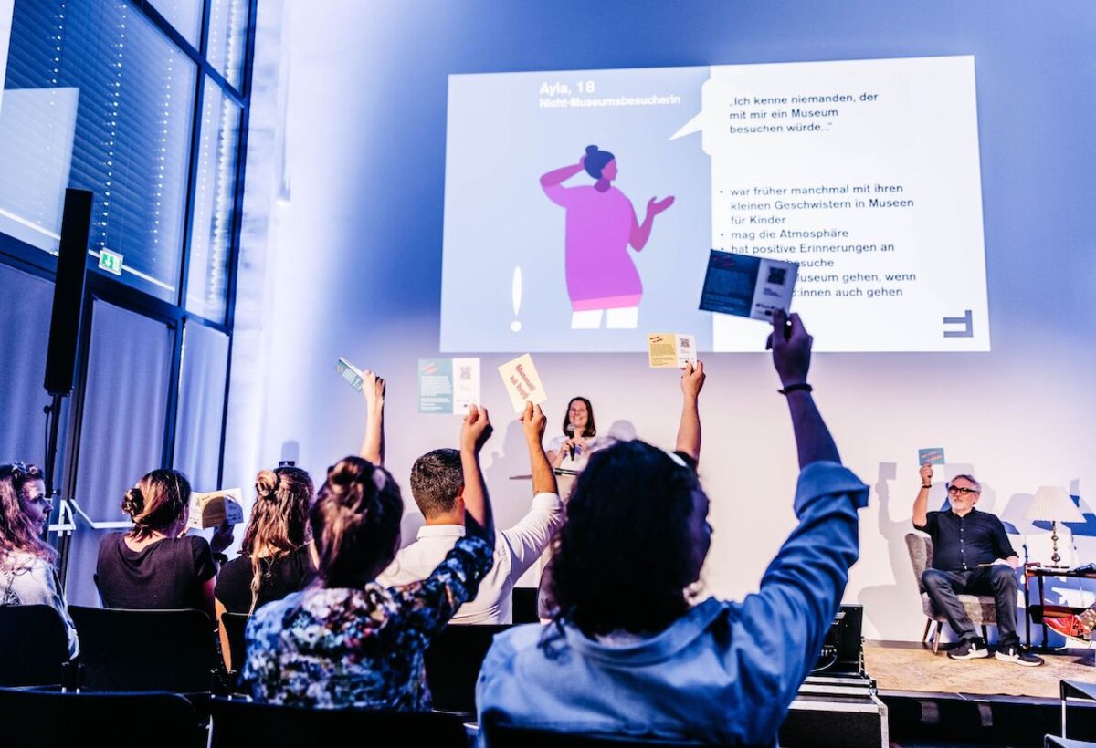 Ein Saal mit Menschen, wo eine Präsentation stattfindet.