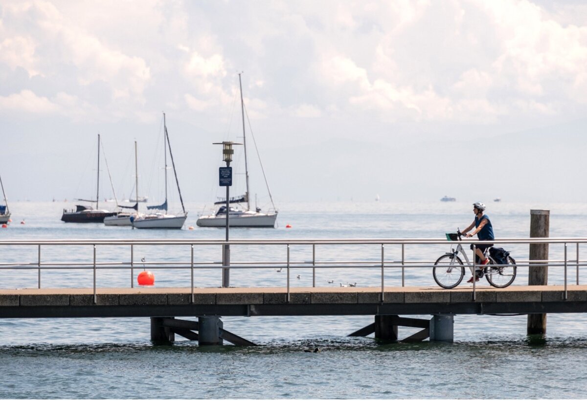 Naturerlebnis am Bodensee mit dem Fahrrad, Frau fährt mit Elektro-Fahrrad auf Bootssteg, weiter Blick auf Bodensee