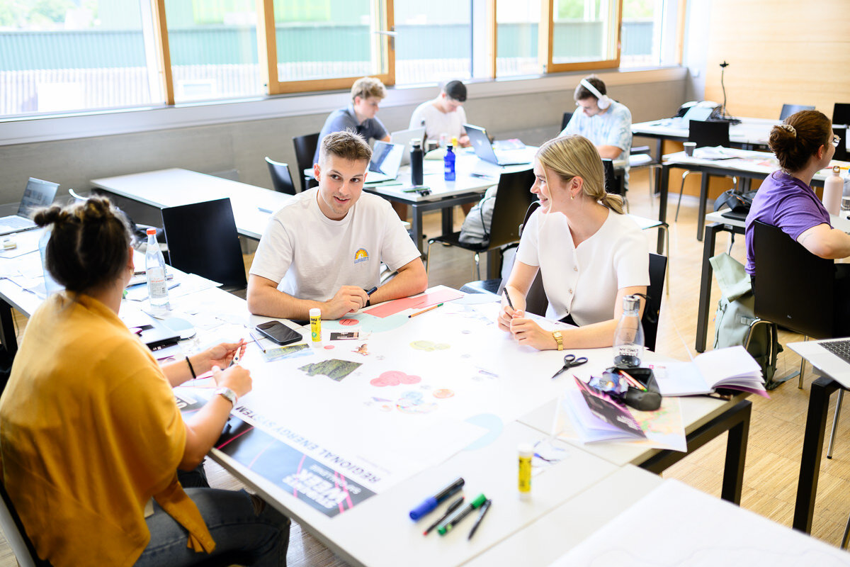 Studierende sitzen an einem Tisch und stellen auf einem Poster ihre Ideen für ein ein nachhaltiges Energiesystem für Vorarlberg dar. | © FHV/Matthias Rhomberg