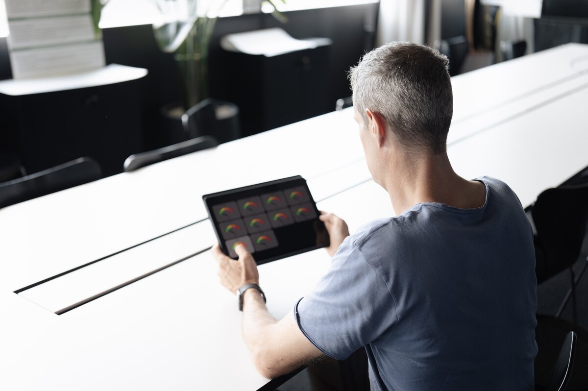 Ein Mann hält ein Tablet in der Hand und steuert damit technische Gebäudefunktionen. Das Bild veranschaulicht das Zusammenspiel von Mensch, digitaler Gebäudetechnik und KI-gestützter Energieoptimierung. | © FHV