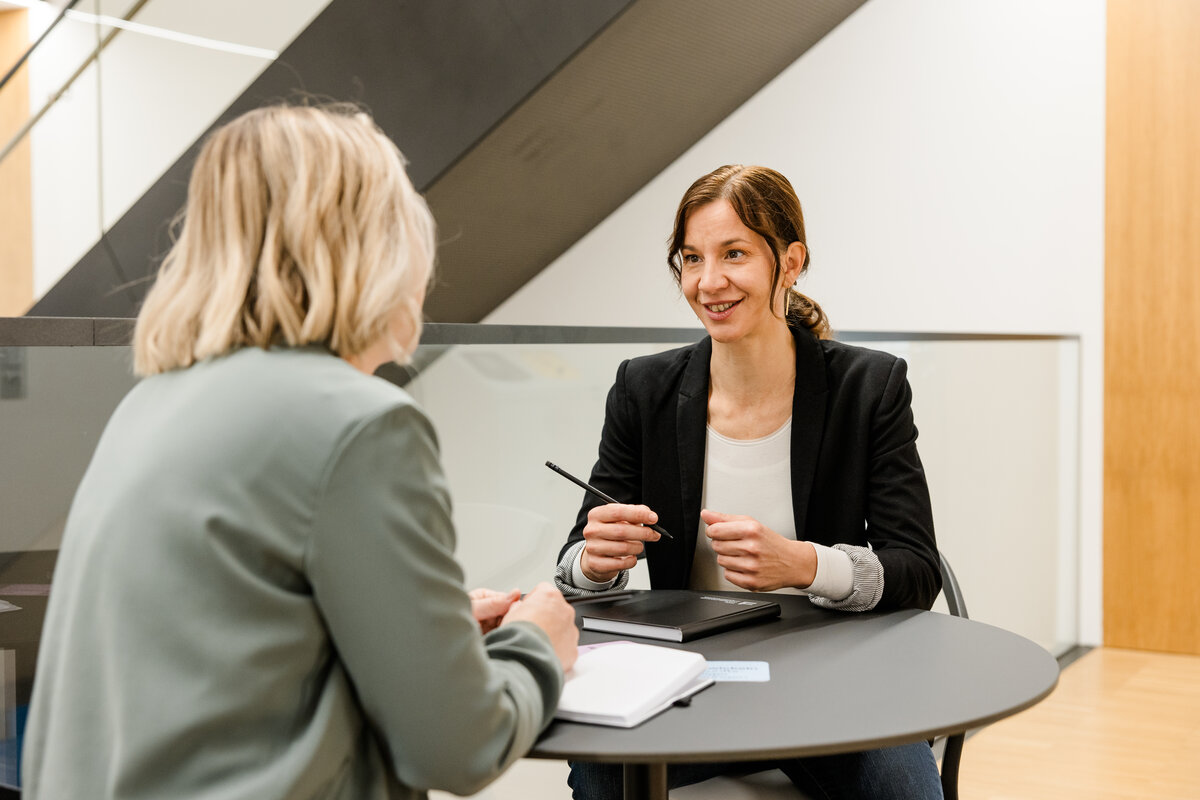 Wissenschaftlerin Katrin Paldán sitzt and einem runden Tisch und unterhält sich mit einer Frau.  | © FHV / Nina Bröll