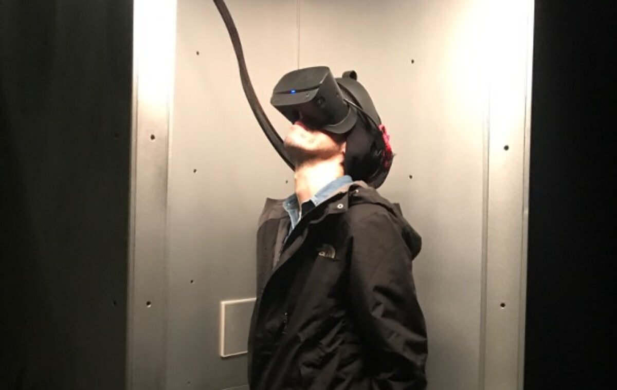 Ein Mann trägt eine VR-Brille und befindet sich in einem engen Raum. Er steht aufrecht, die Arme leicht angehoben, während er in die virtuelle Umgebung eintaucht. | © FHV