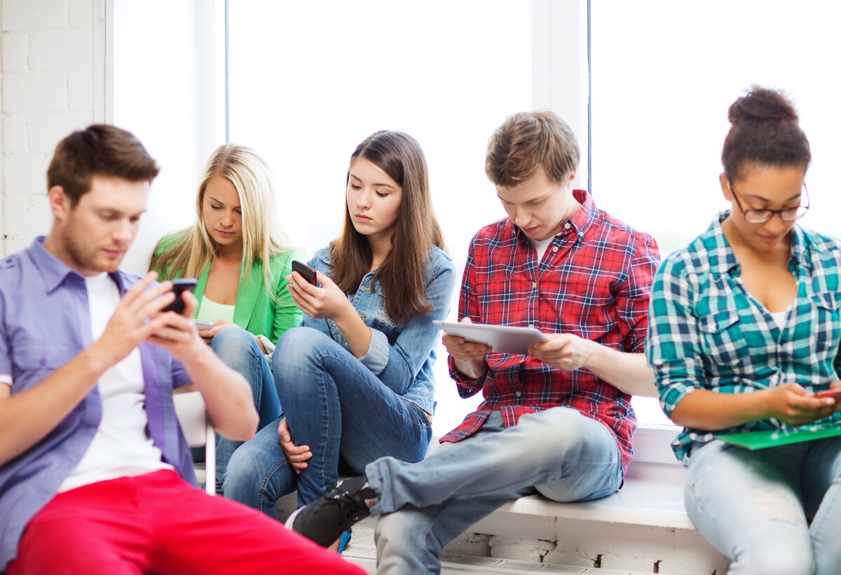 Jugendliche sitzen am Boden in einer Gruppe und haben das Handy in der Hand.