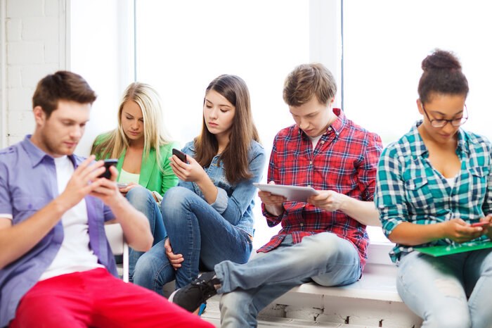 Jugendliche sitzen am Boden in einer Gruppe und haben das Handy in der Hand. | © FHV