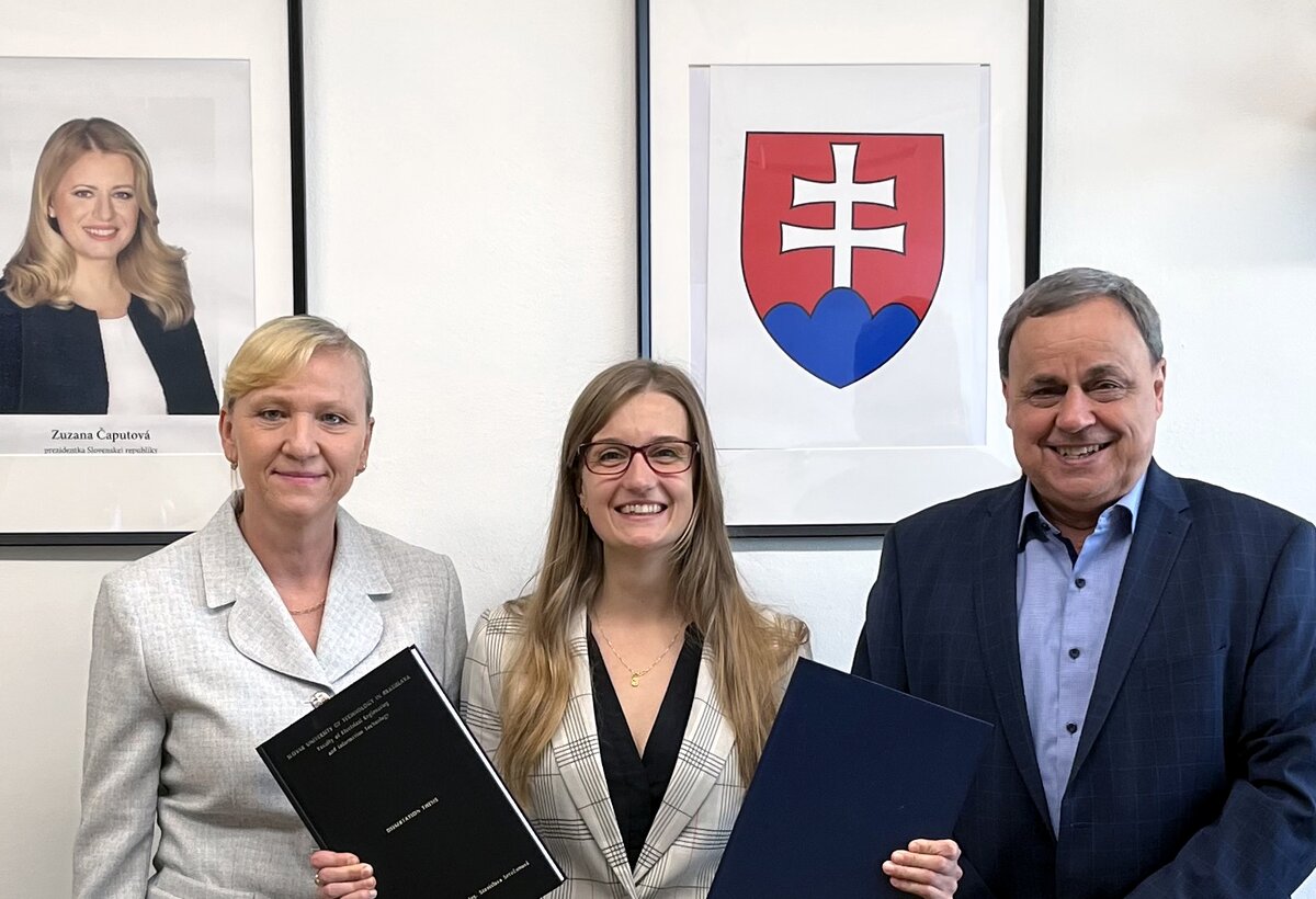 Gruppenfoto von drei Personen. Die mittlere Person hält ihre Dissertation in den Händen.