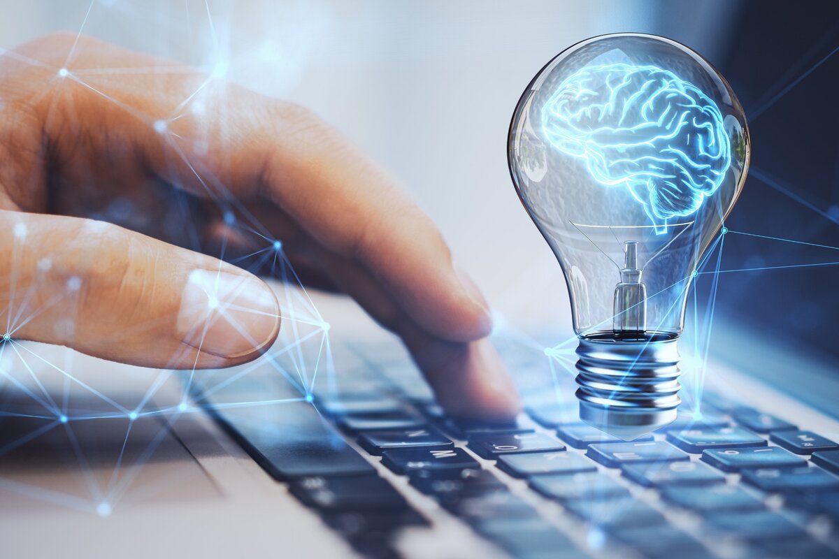 Hand über Tastatur, darüber schwebt eine leuchtende Glühbirne mit blauem Gehirn als Symbol für kreative Ideen. | © Adobe Stock