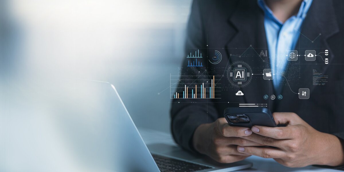 Person sitzt vor Laptop und hält ein Smartphone, über ihr schweben futuristische Symbole für KI, Cloud und Datenanalyse. | © Adobe Stock