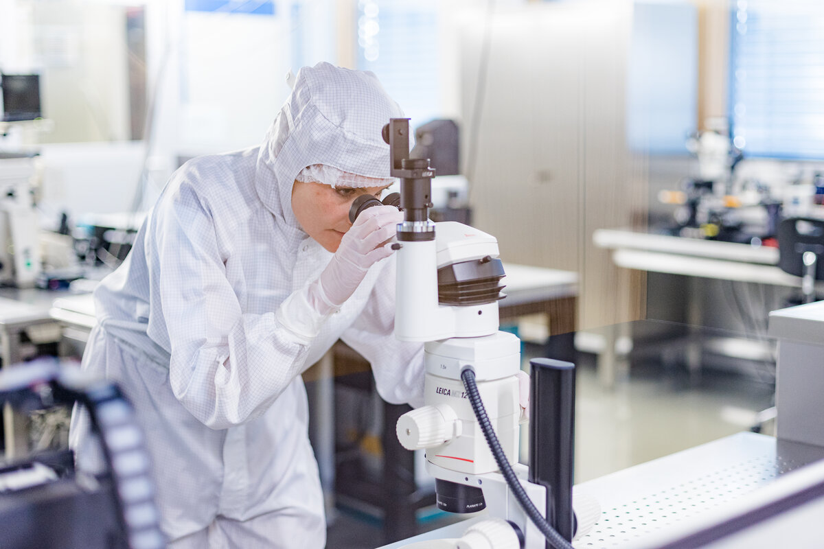 Eine Frau im Schutzanzug blickt in ein Mikroskop | © Nina Bröll / FHV