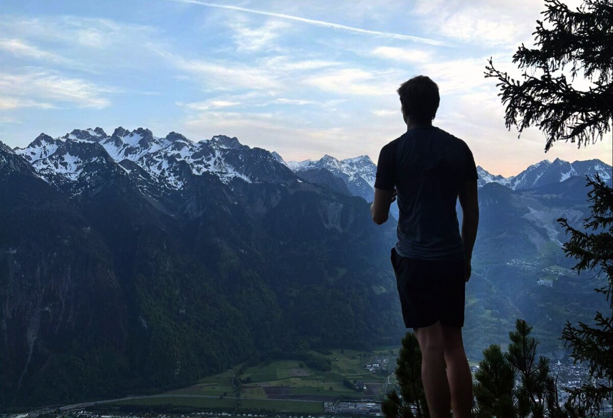 Dusky dark silouette of a person in the foreground with deep blue Alpine scenery in the background. | © FHV