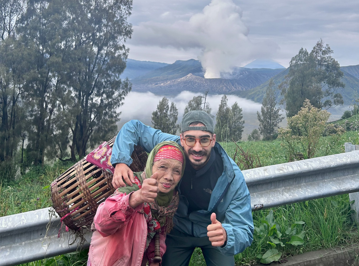 Ibrahim steht mit einer einheimischen Frau auf Bali, Indonesien, vor einem rauchenden Vulkan. Die Szene zeigt die exotische Landschaft Balis und die beeindruckende vulkanische Natur der Insel. | © Privat