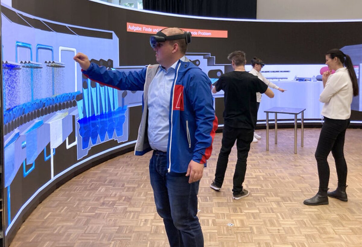 Mann mit VR-Brille steht vor einer Wand und streckt die Hand aus | © FHV