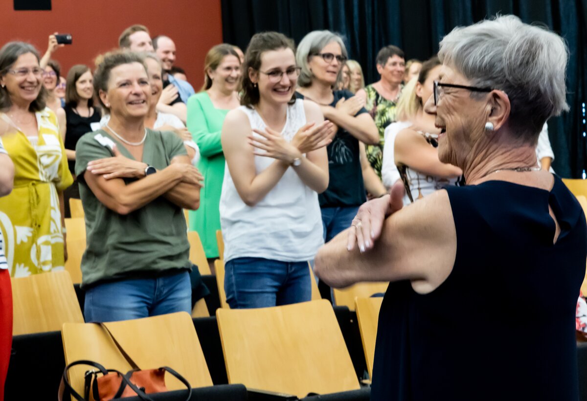 Teilnehmende, hauptsächlich Frauen, beim uDay an der Fachhochschule Vorarlberg im Juni 2023. Eine Frau rechts im bild vom Aphasie-Chor macht Bewegungen vor, die Gäste machen es nach und lachen herzlich. | © FHV-Karin-Trommelschläger