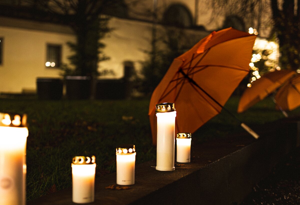 Brennende Kerzen und ein oranger Regenschirm im Hintergrund
