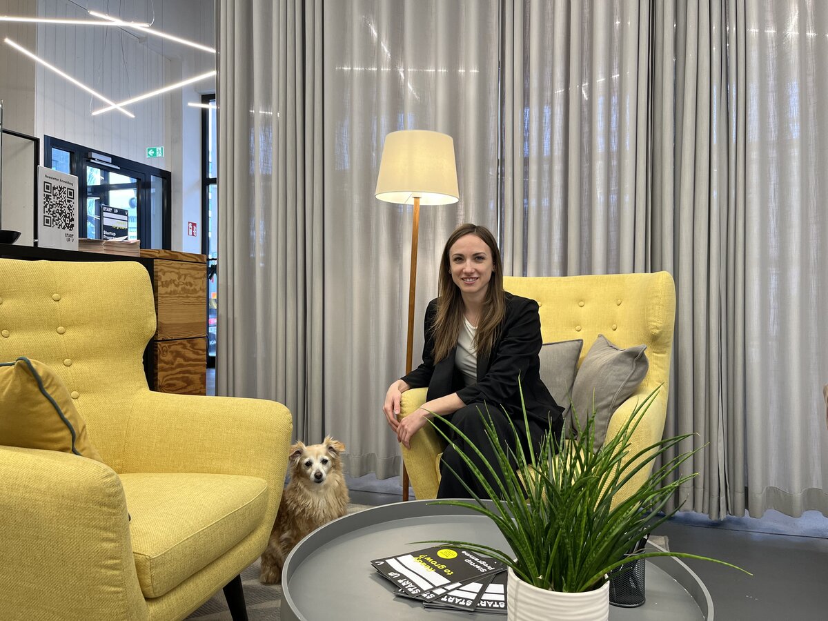 Frau sitzt in einem Interview-Setup in einer Lounge auf einem gelben Sessel, neben ihr sitzt ihr Hund. | © FHV