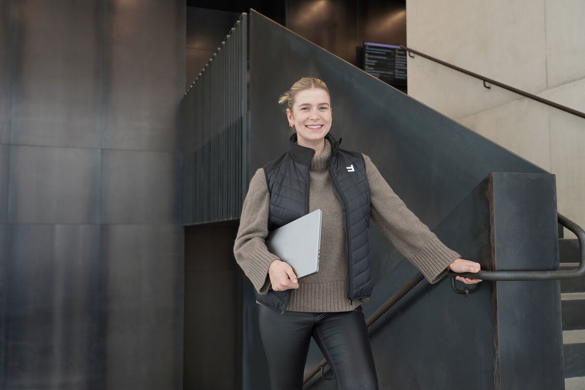 Julia Ilg steht mit ihrem Laptop im Treppenhaus des FHV-Gebäudes. | © FHV
