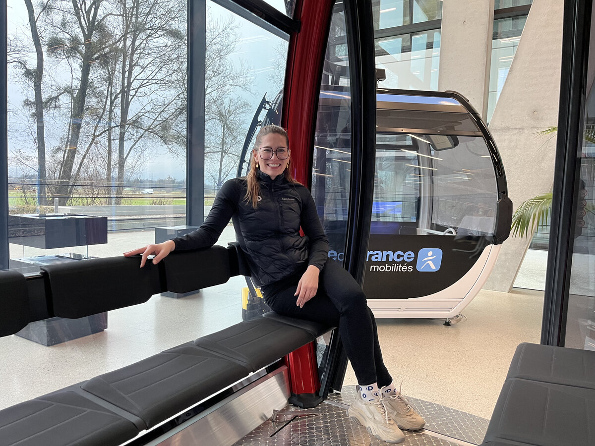 Stefanie Huber sitzt in einer roten Doppelmayr Gondel im Ausstellungsraum des Unternehmens. | © FHV