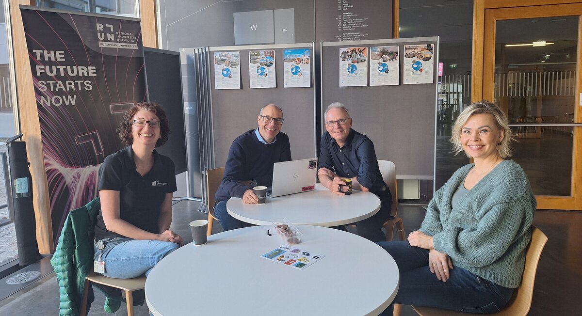 Sabine Frick sitzt mit Kollegen vor einem RUN-EU Pop-up Banner bei der RUN-EU Infoveranstaltung. | © FHV