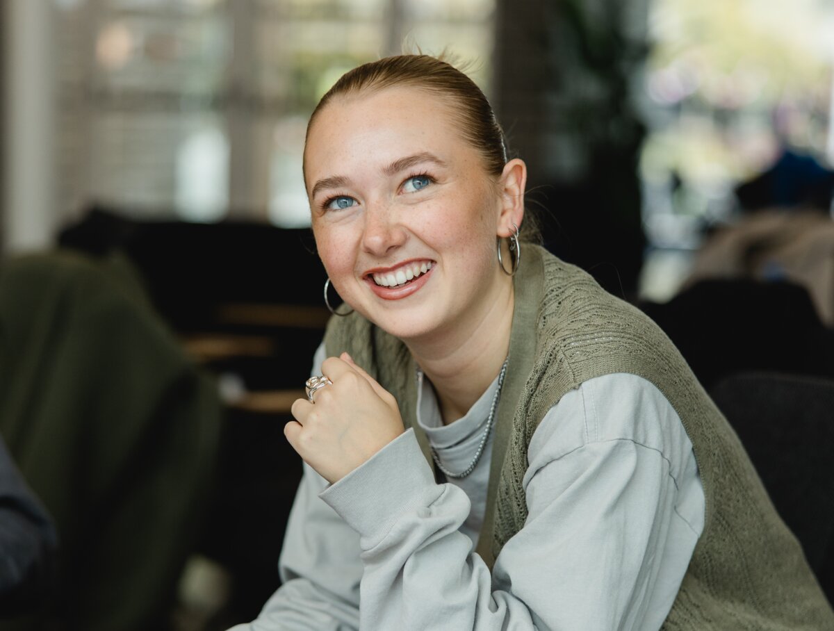 Studentin Hannah lächelt in die Kamera währende sie im Cafe Campus am lernen ist. | © Nina Broell | FHV