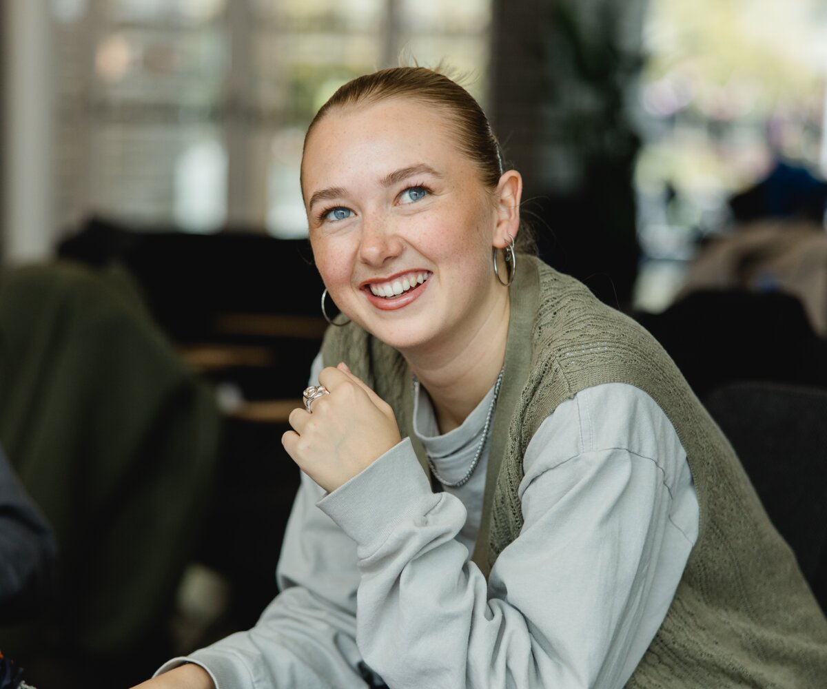 Studentin Hannah lächelt in die Kamera währende sie im Cafe Campus am lernen ist. | © Nina Broell | FHV