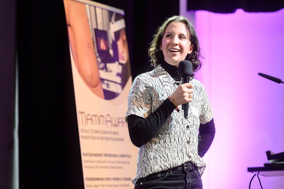 FHV-Studentin hält Vortrag auf der Bühne und steht vor einem Standup-Banner mit dem Schriftzug MammAware. | © Rhomberg | FHV