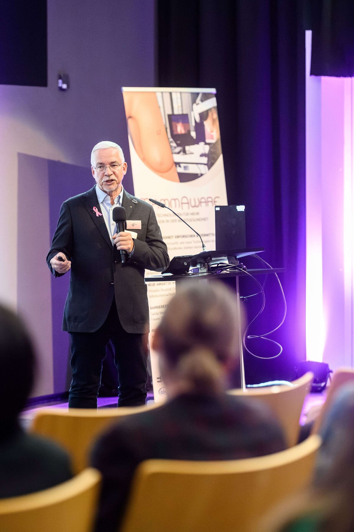 Dr. Frank Hoffmann hält einen Vortrag auf der Bühne. Im Vordergrund ist das Publikum von hinten zu sehen. | © Rhomberg | FHV