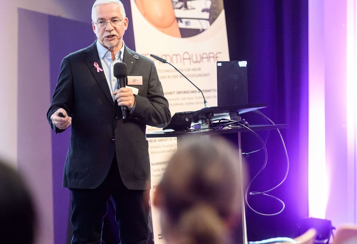 Dr. Frank Hoffmann hält einen Vortrag auf der Bühne. Im Vordergrund ist das Publikum von hinten zu sehen. | © Rhomberg | FHV