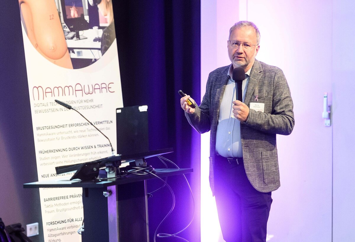 Dr. Bernd Hartmann steht auf der Bühne und spricht vor dem Standup-Banner mit dem Schriftzug ‚MammAware‘. | © Rhomberg | FHV