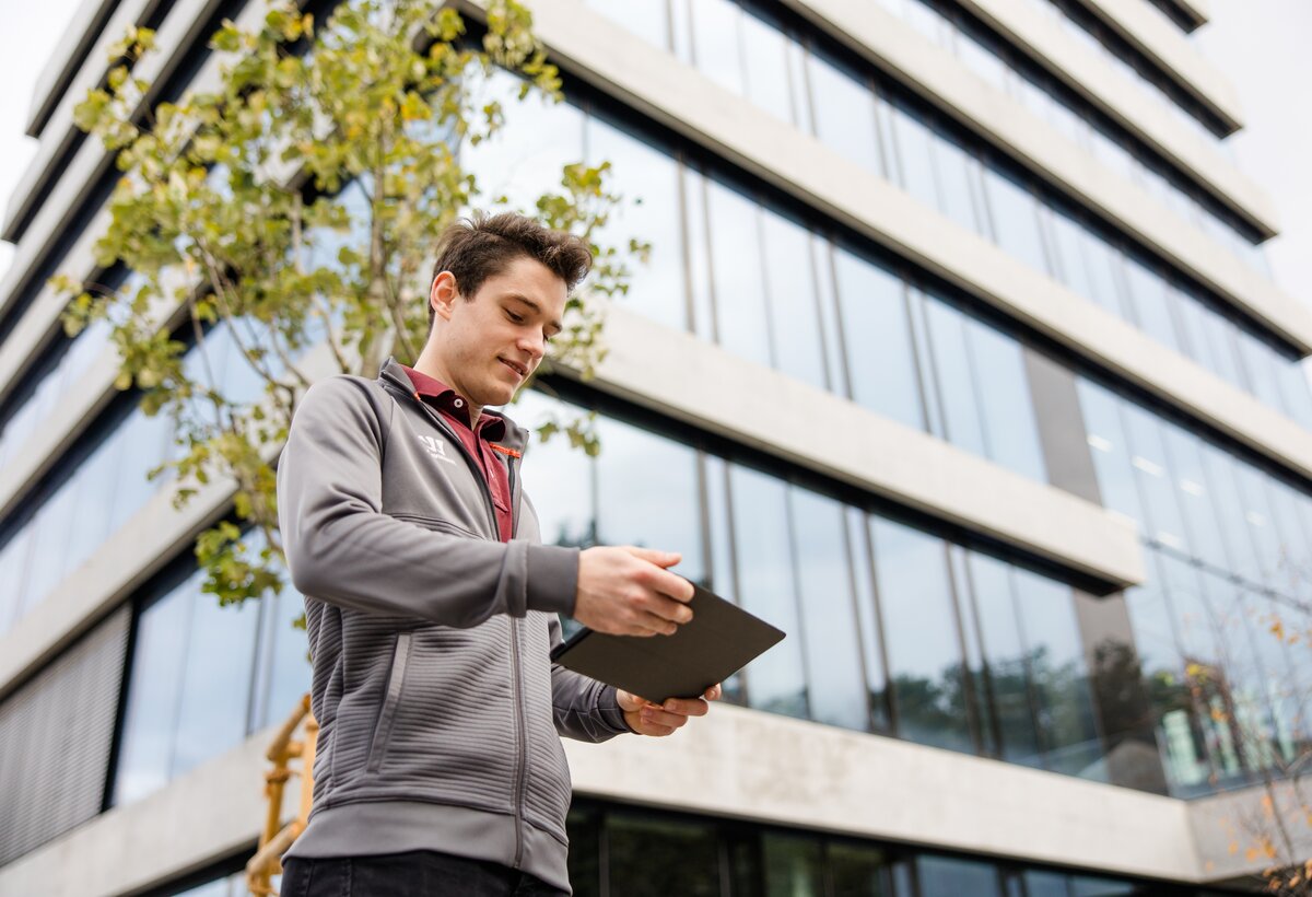 Studentambassador Tobias Wenzel vor dem FHV Gebäude mit einem Tablett in der Hand. | © Broell