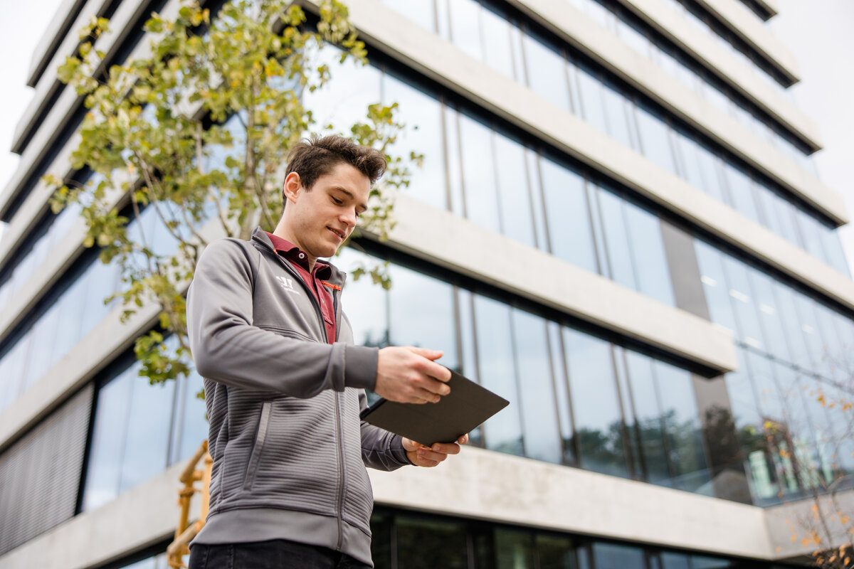 Studentambassador Tobias Wenzel vor dem FHV Gebäude mit einem Tablett in der Hand. | © Broell