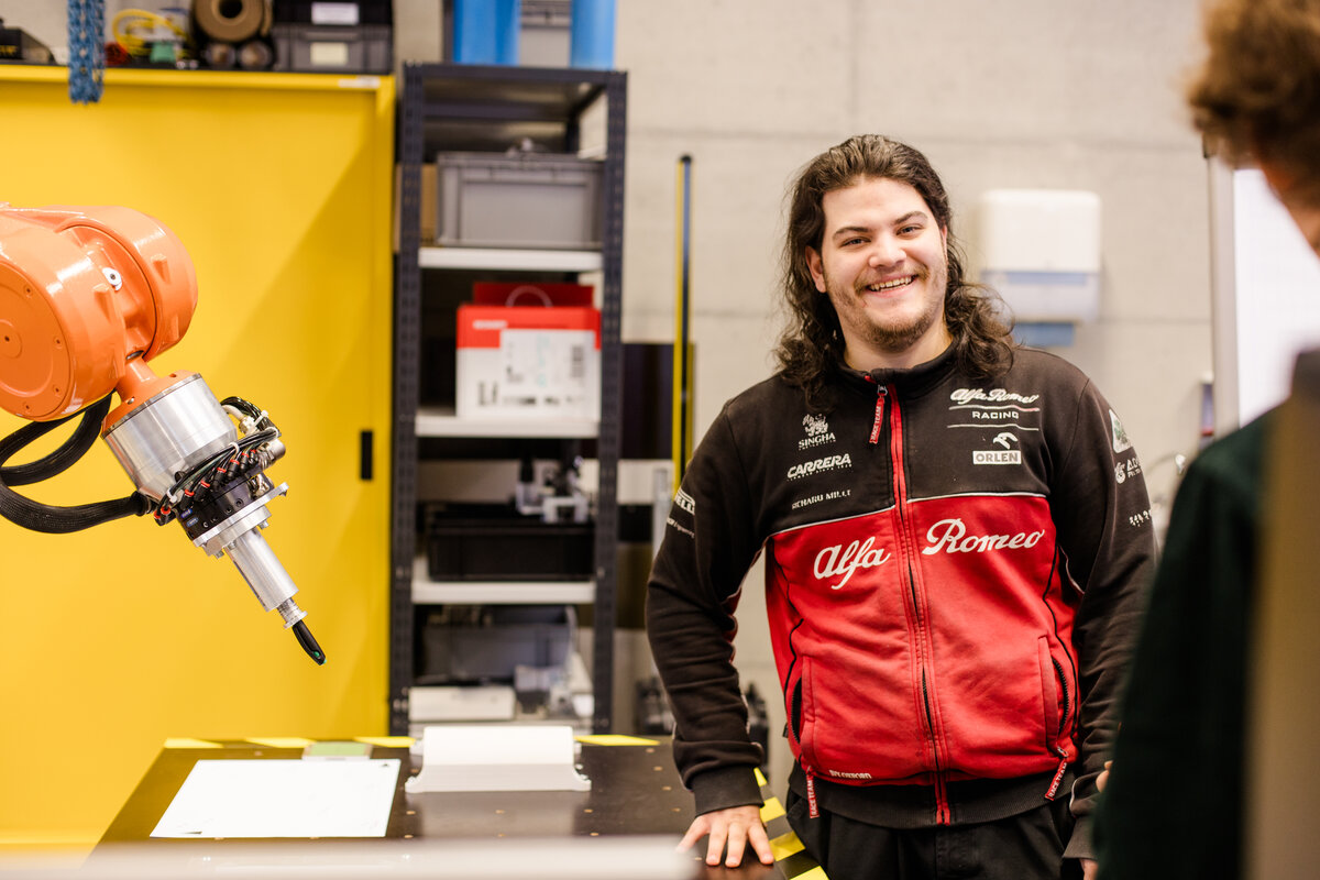 Student Jean Philipp steht im Labor. Links neben ihm ist ein Roboterarm zu sehen. | © Nina Broell