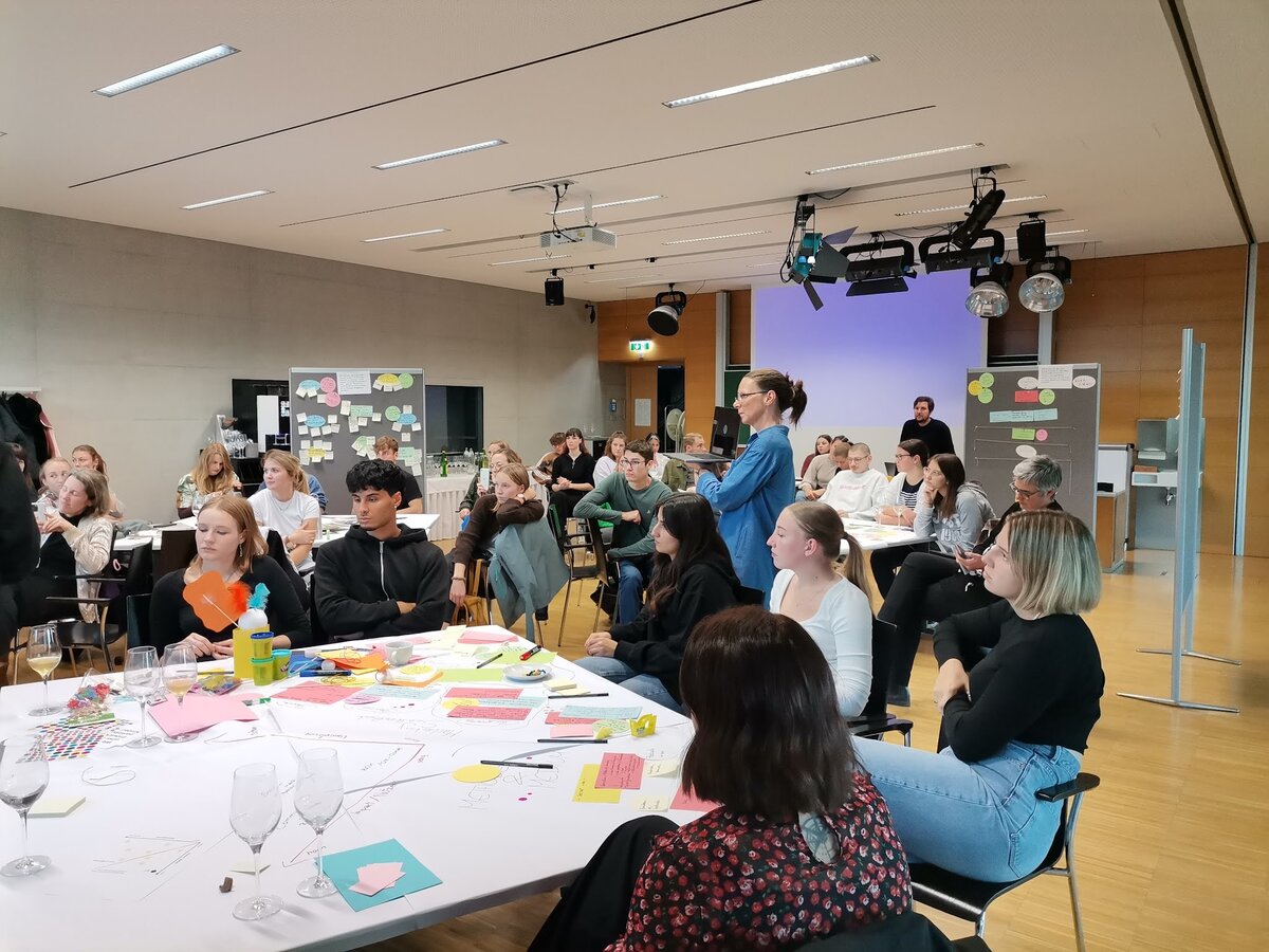 sitzende Personen um einen Tisch mit vielen bunten Papieren und Präsentationspaneelen | © ©fachbereich-gestaltung-fhv